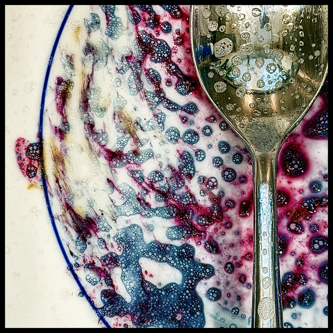 An abstract close-up of a plate with deep purple and blue food residue and a silver spoon